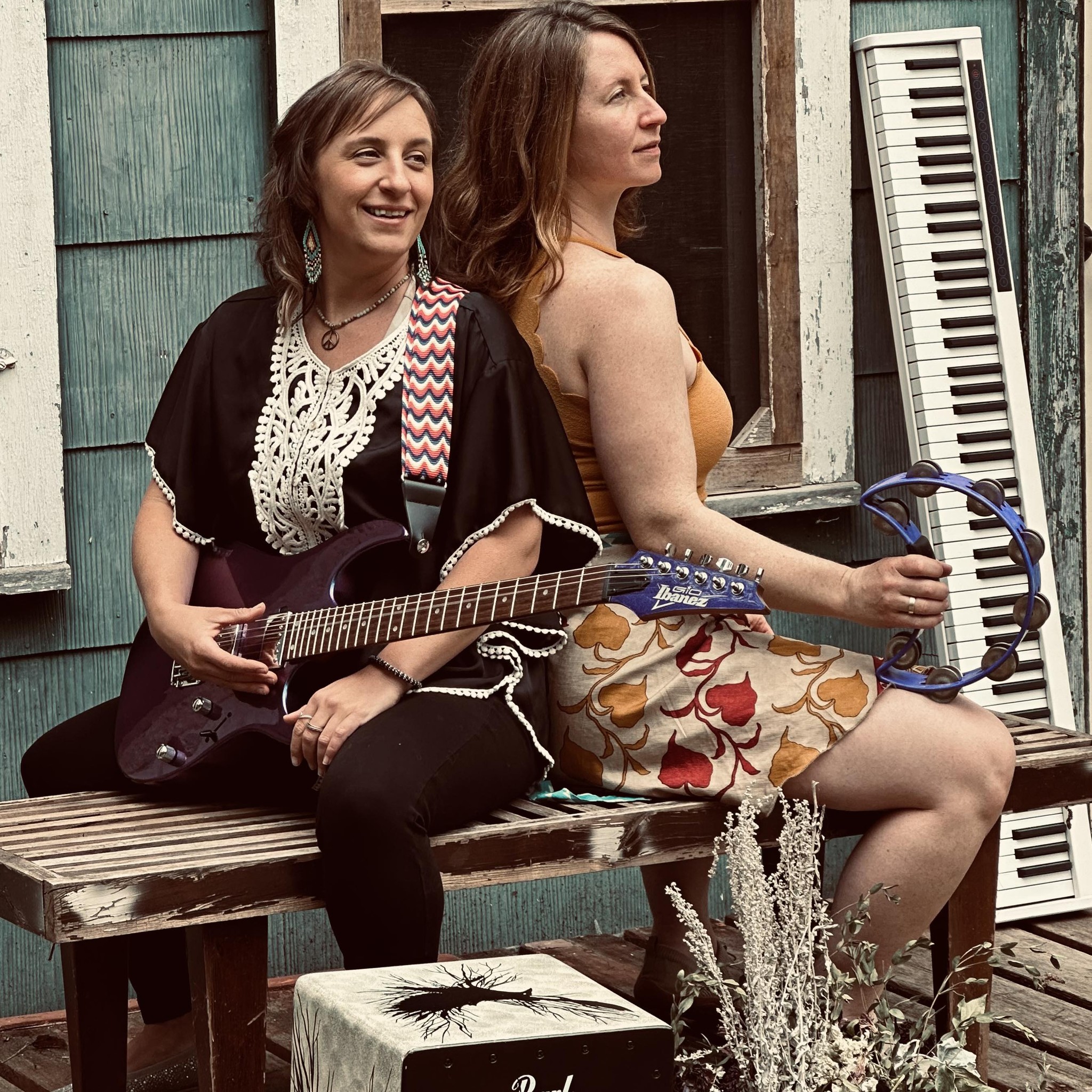 Carolyn Jo with electric guitar and Joni Clare with tambourine on a weathered porch.